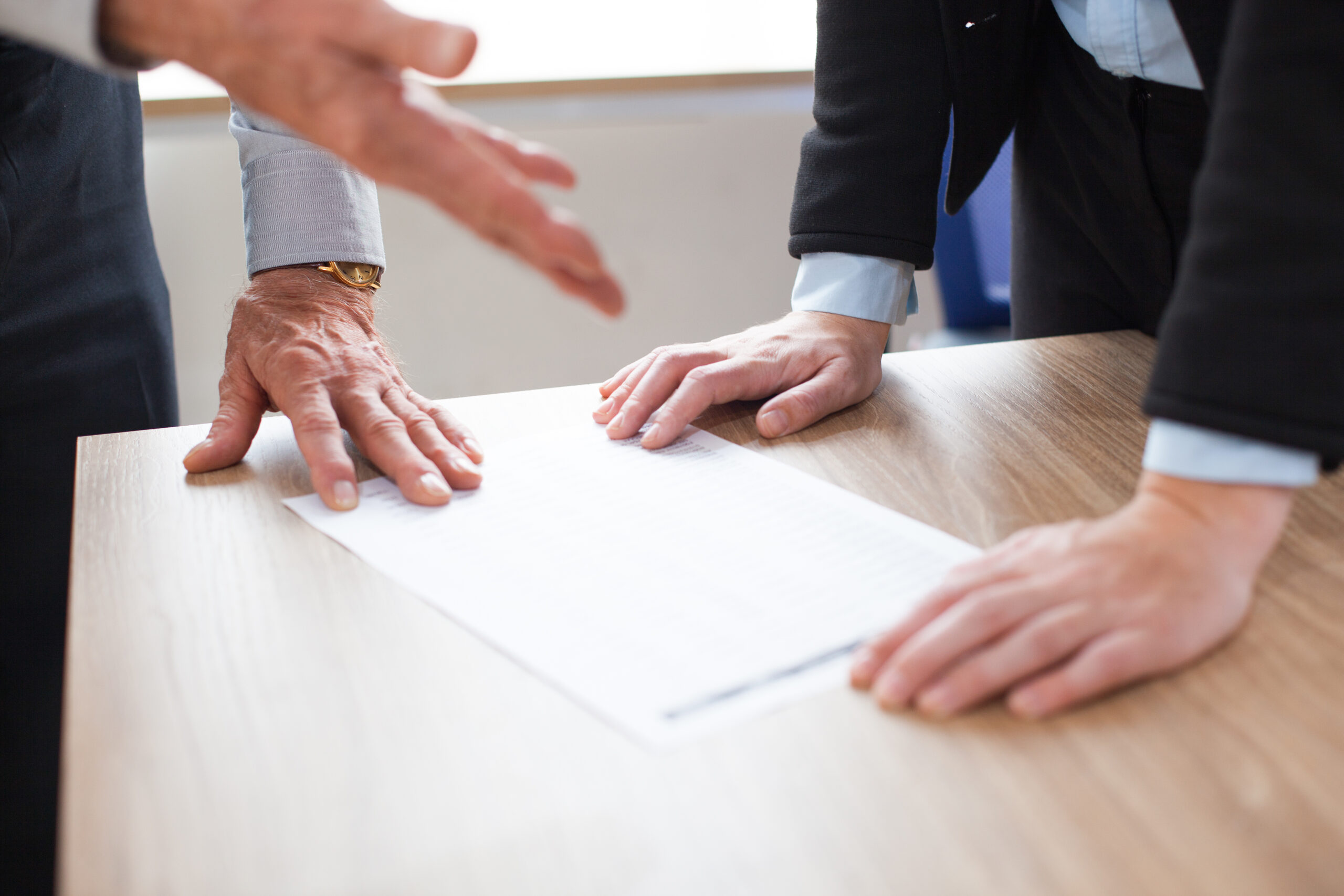 Unrecognizable business people discussing document. One person gesturing, other leaning on table. Business paper on desk. Teamwork concept