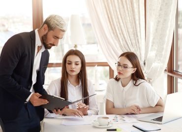 Restaurant director is showing financial diagrams in the documents and two assistants girls are listening with attention